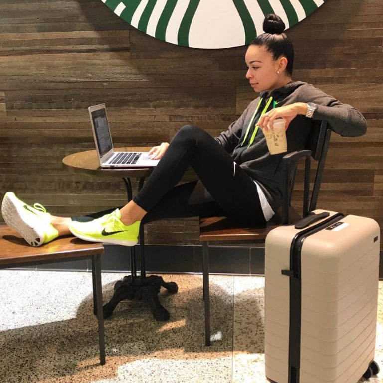 Woman with laptop, coffee, luggage.